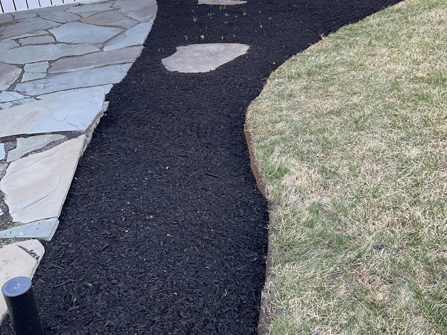 Sweeping black mulch bed edging a flagstone walkway beside a home