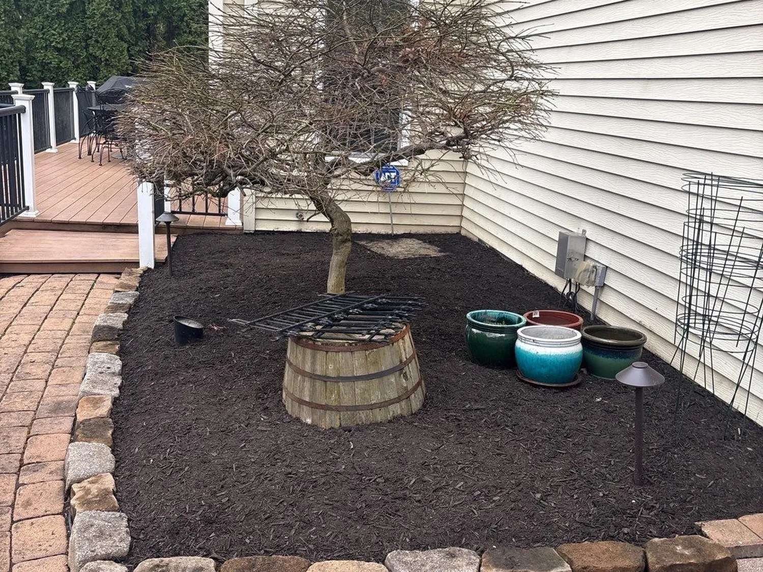 Brown mulch bed with a natural stone border beside a paver patio and ornamental tree