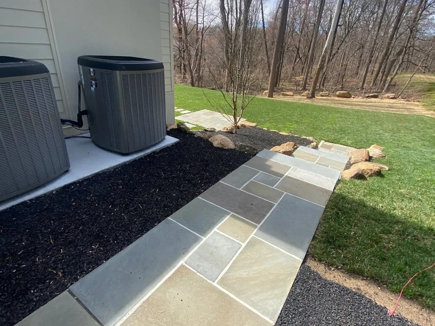 Dark mulch bed lining a bluestone flagstone walkway leading toward a wooded backyard