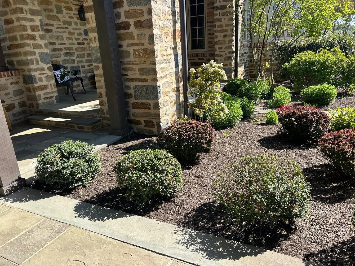Stone-home foundation bed with boxwood shrubs and freshly spread mulch by the front entry